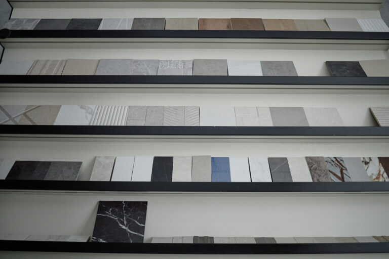 Multiple rows of ceramic and stone tile samples arranged on wall-mounted shelves, showcasing various textures and patterns for interior design or architectural selection purposes