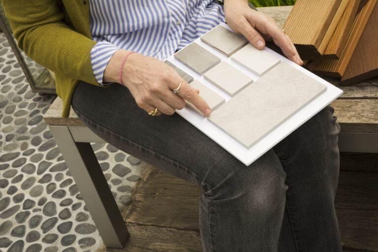 High angle view of woman sitting on garden bench, holding tile samples.